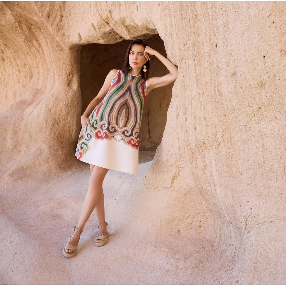 Woman wearing sleeveless A-line linen dress with artistic multicolor print, styled in natural cave setting for summer or resort fashion