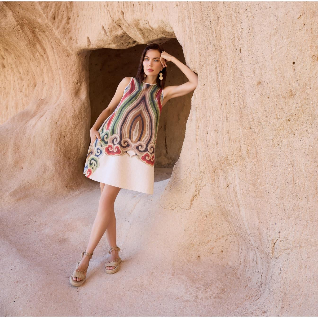 Woman wearing sleeveless A-line linen dress with artistic multicolor print, styled in natural cave setting for summer or resort fashion