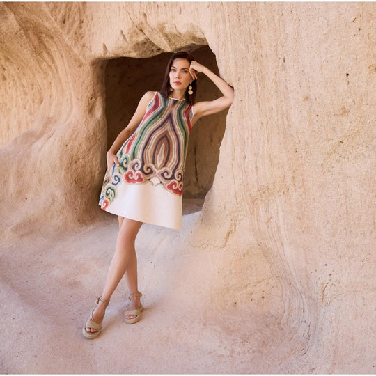Woman wearing sleeveless A-line linen dress with artistic multicolor print, styled in natural cave setting for summer or resort fashion