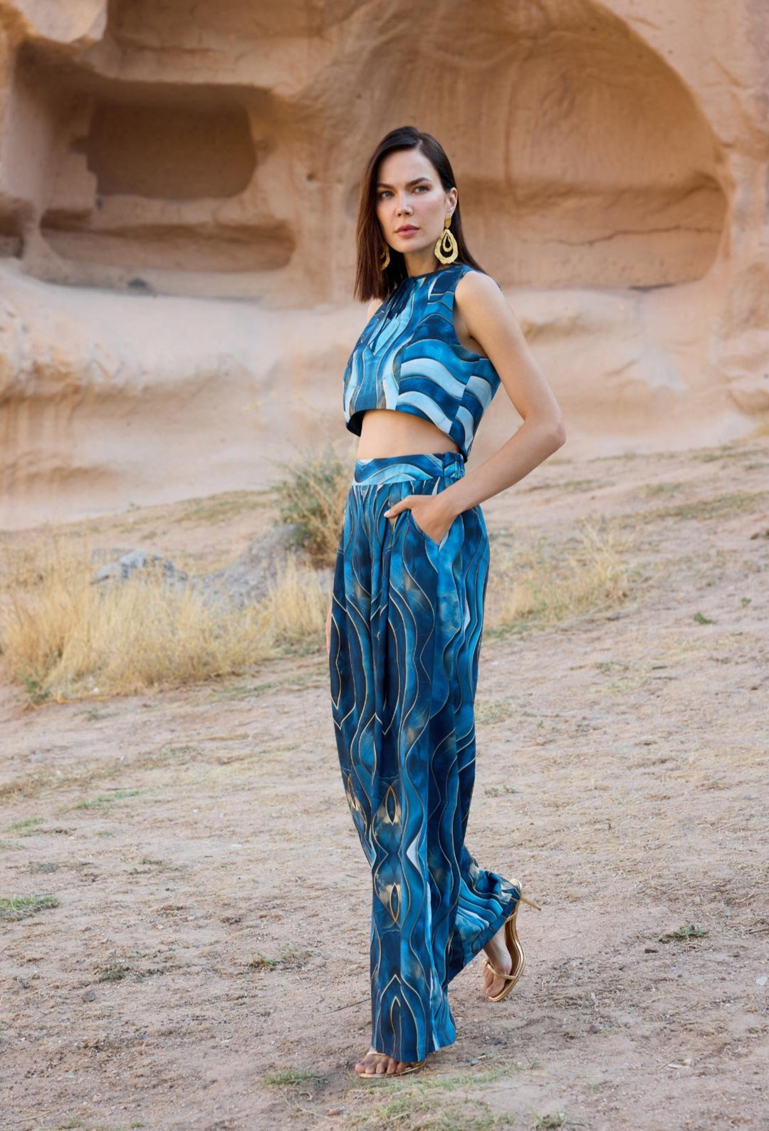 Woman in a blue outfit standing in a desert landscape with rock formations.